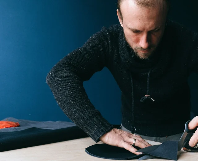 Tailor cutting leather at a workbench, the first step in making custom varsity jackets