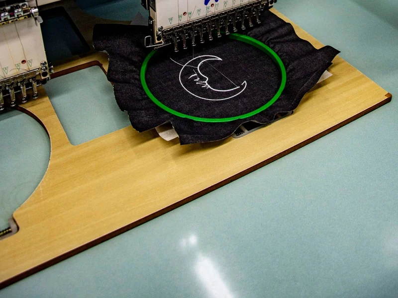 Industrial embroidery machine stitching a design on dark fabric in a hoop