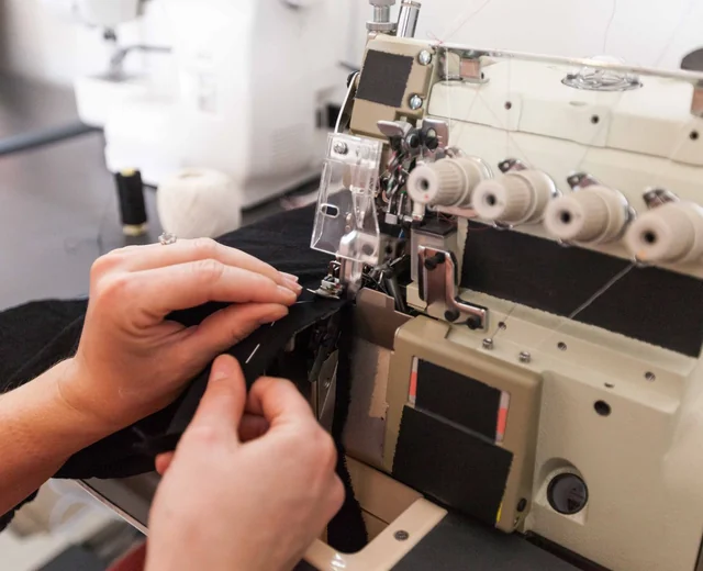 Hands guiding black fabric through an overlock machine during hoodie construction