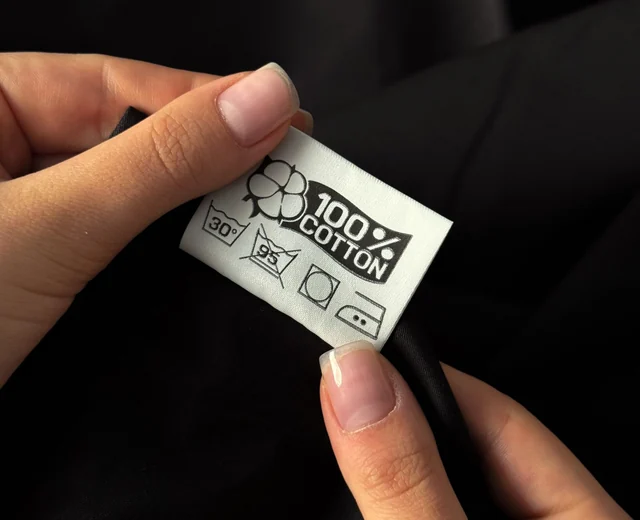 Hands holding a printed 100% cotton care label with washing symbols